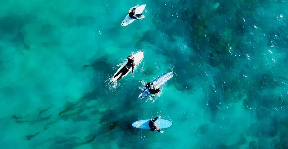 Aerial view of four surfers paddling over clear turquoise water and reef