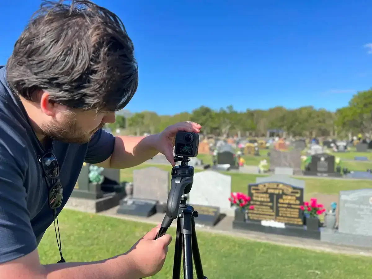 A Mobiddiction team member setting up a 360-degree camera on a tripod among headstones