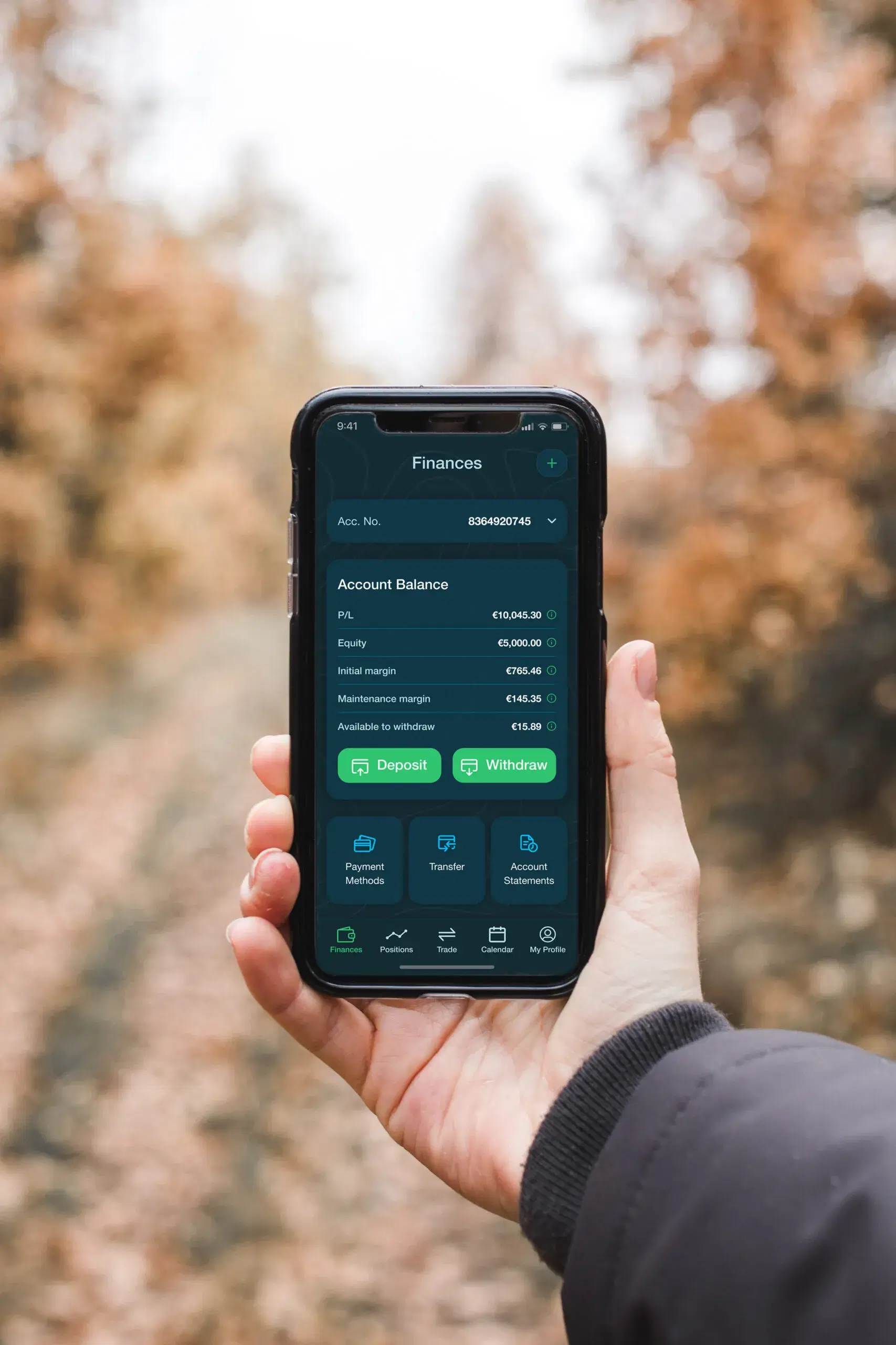 Hand holding a phone showing a trading app’s account balance, margin figures and deposit and withdraw buttons