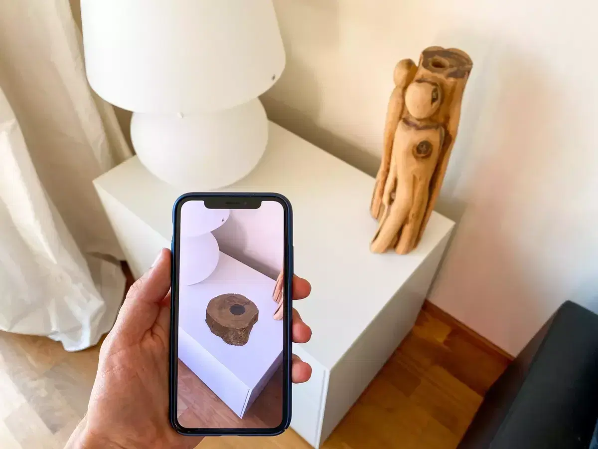 Phone placing a 3D wooden object onto a white plinth in augmented reality