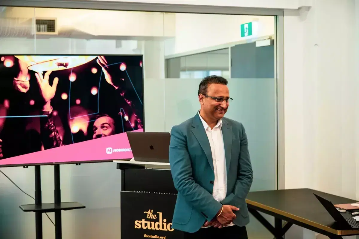Mobiddiction founder Mike Vasavada smiling beside a presentation screen at a studio event