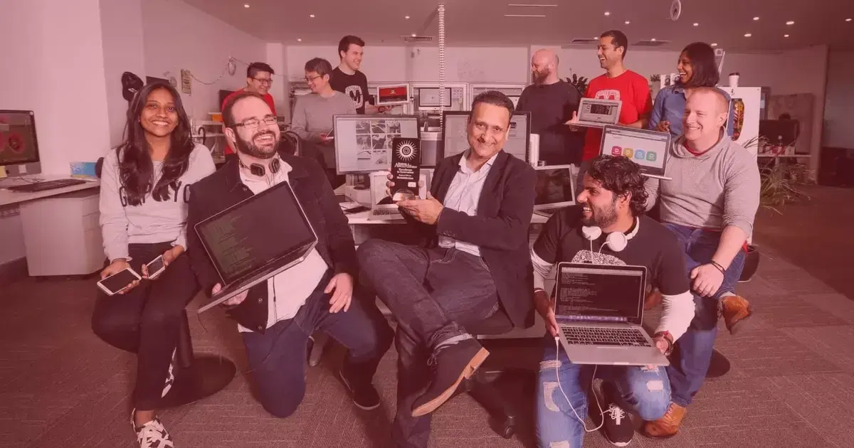 Mobiddiction team members gathered in the office with laptops, phones and an award trophy