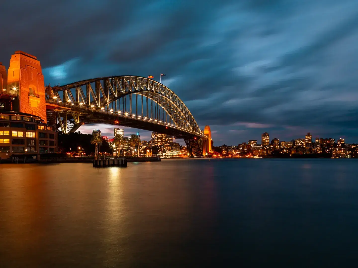 The Sydney Harbour Bridge lit up at dusk, reflected in the harbour