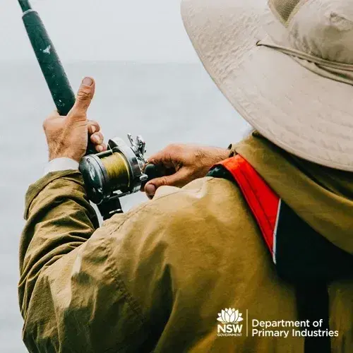 A recreational fisher in a wide-brimmed hat and jacket reeling in a line