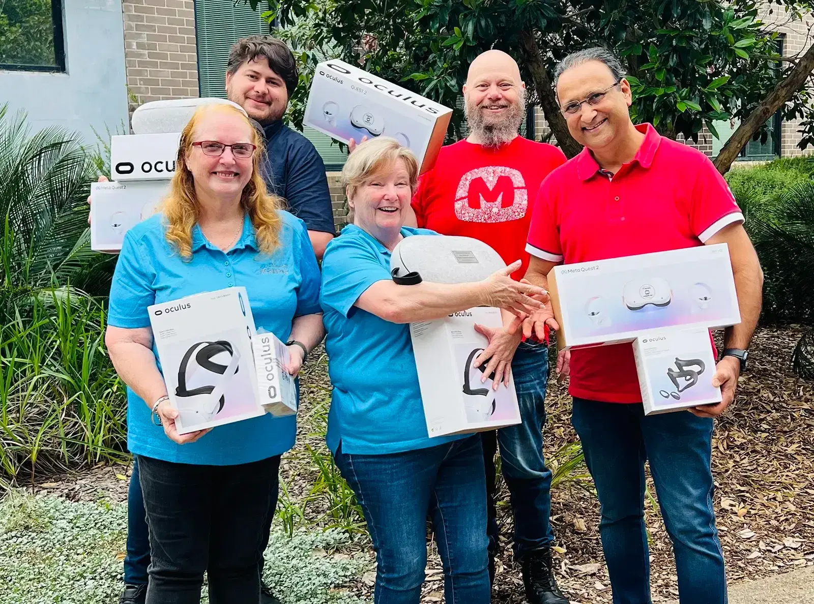 Mobiddiction and partner team members outdoors, smiling and holding boxes of Meta Quest 2 VR headsets