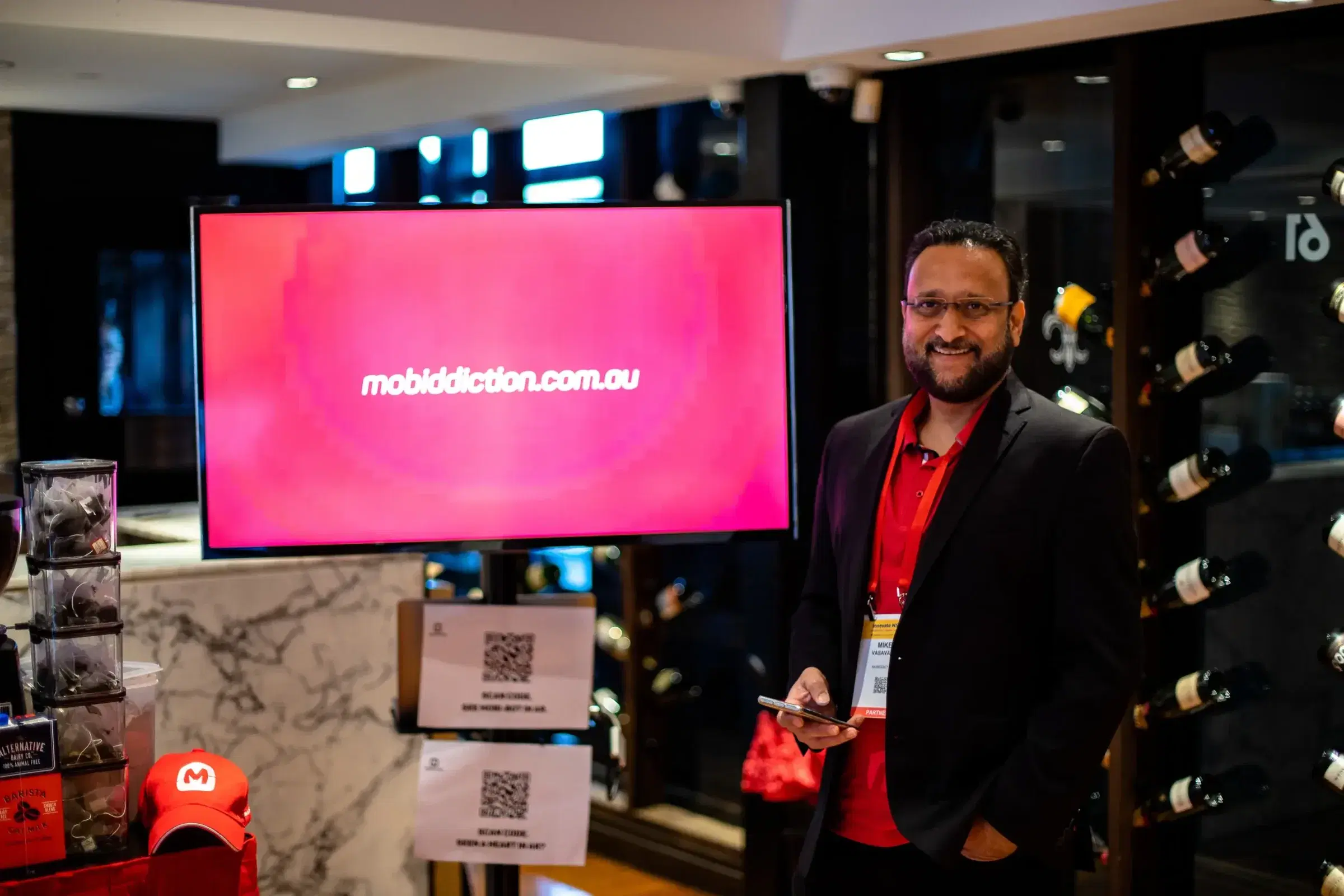 Mike Vasavada, Mobiddiction’s director, beside a screen showing mobiddiction.com.au at a government industry event