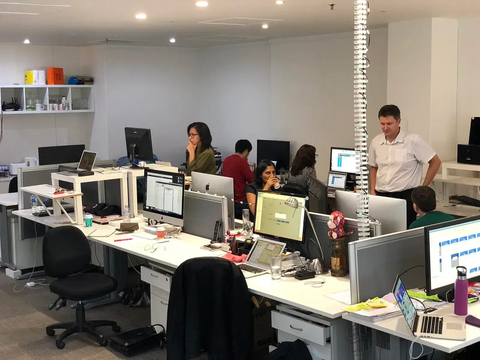 The Mobiddiction team at work across the Sydney office floor, one engineer standing at a colleague’s desk