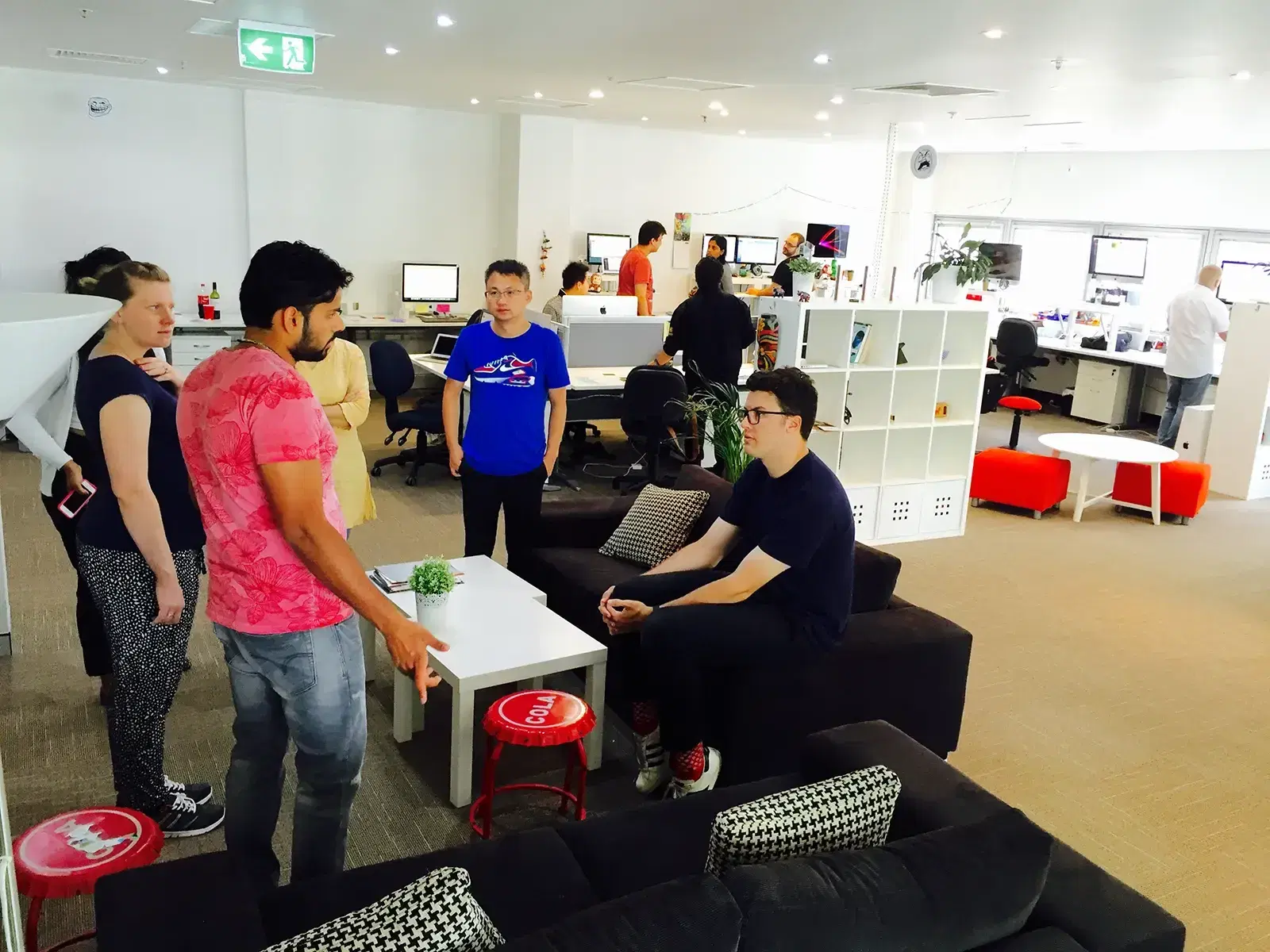 Mobiddiction team members talking around a lounge area in the Sydney office, with desks and monitors behind